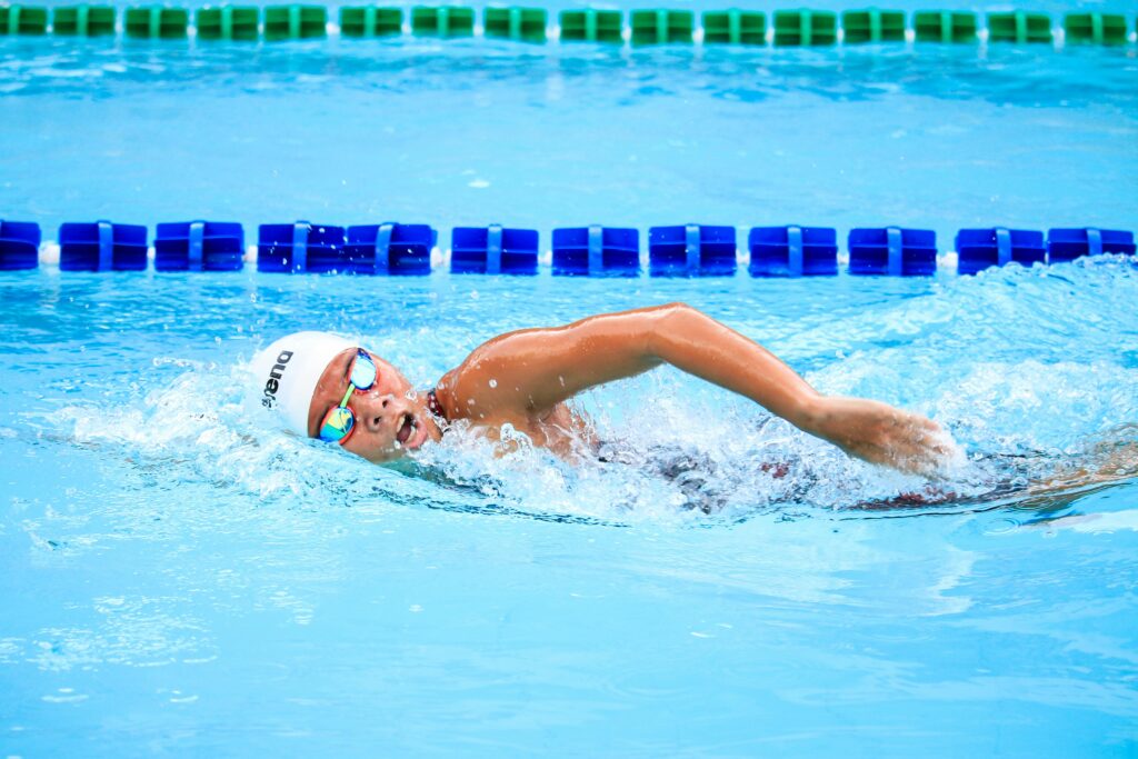 A swimmer energetically performs a freestyle stroke in a clear outdoor swimming pool, showcasing competitive spirit.