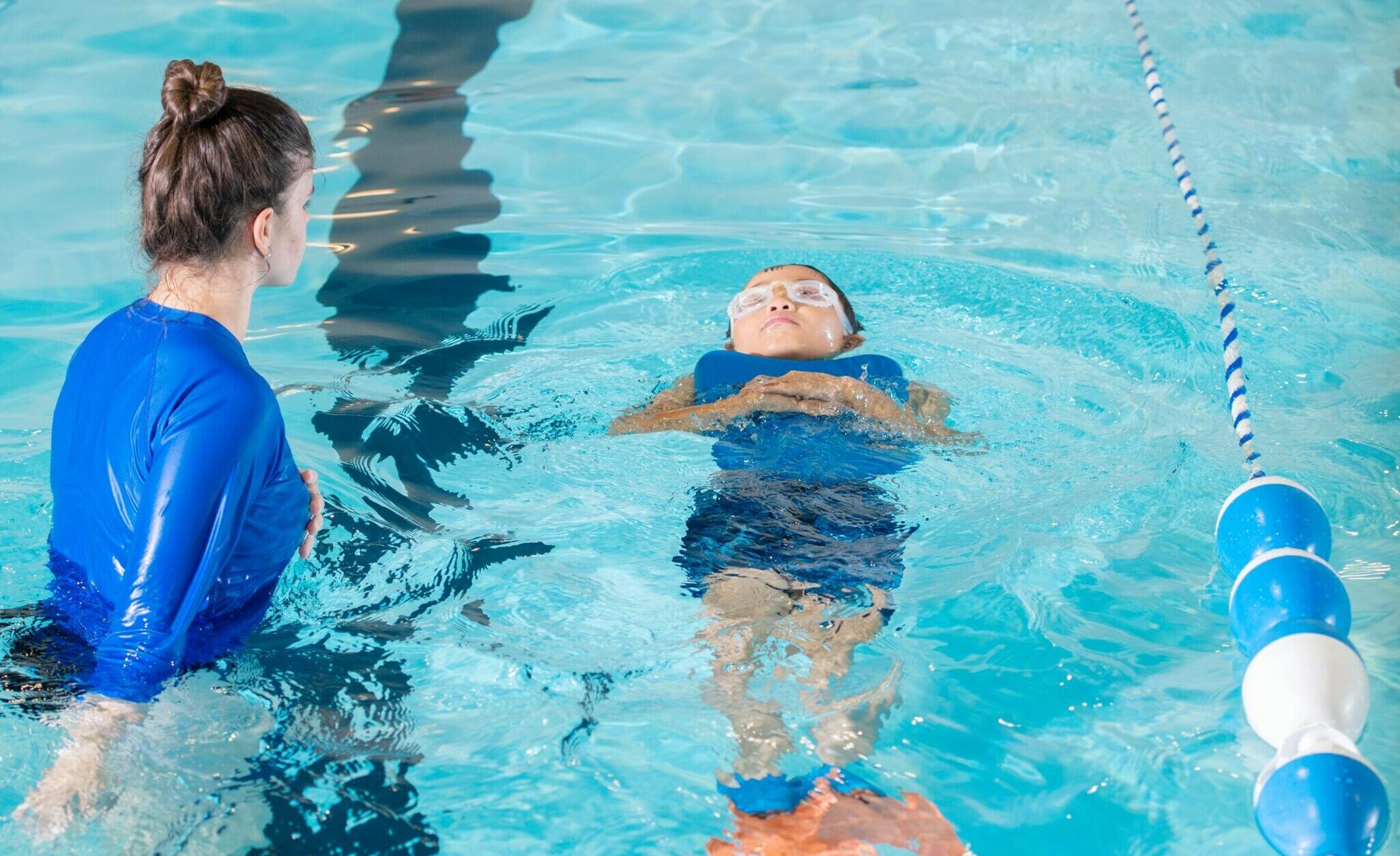A swimming instructor teaches a young child to swim in an indoor pool.