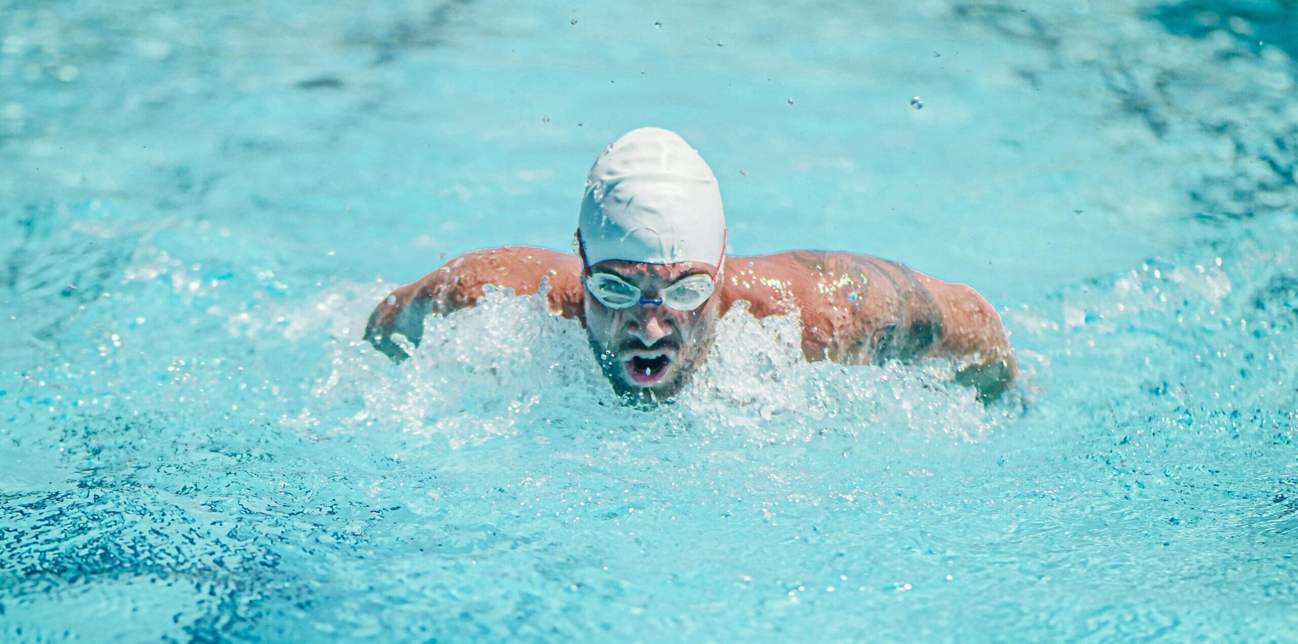 A determined male swimmer performing a butterfly stroke in a clear blue pool, embodying fitness and athleticism.
